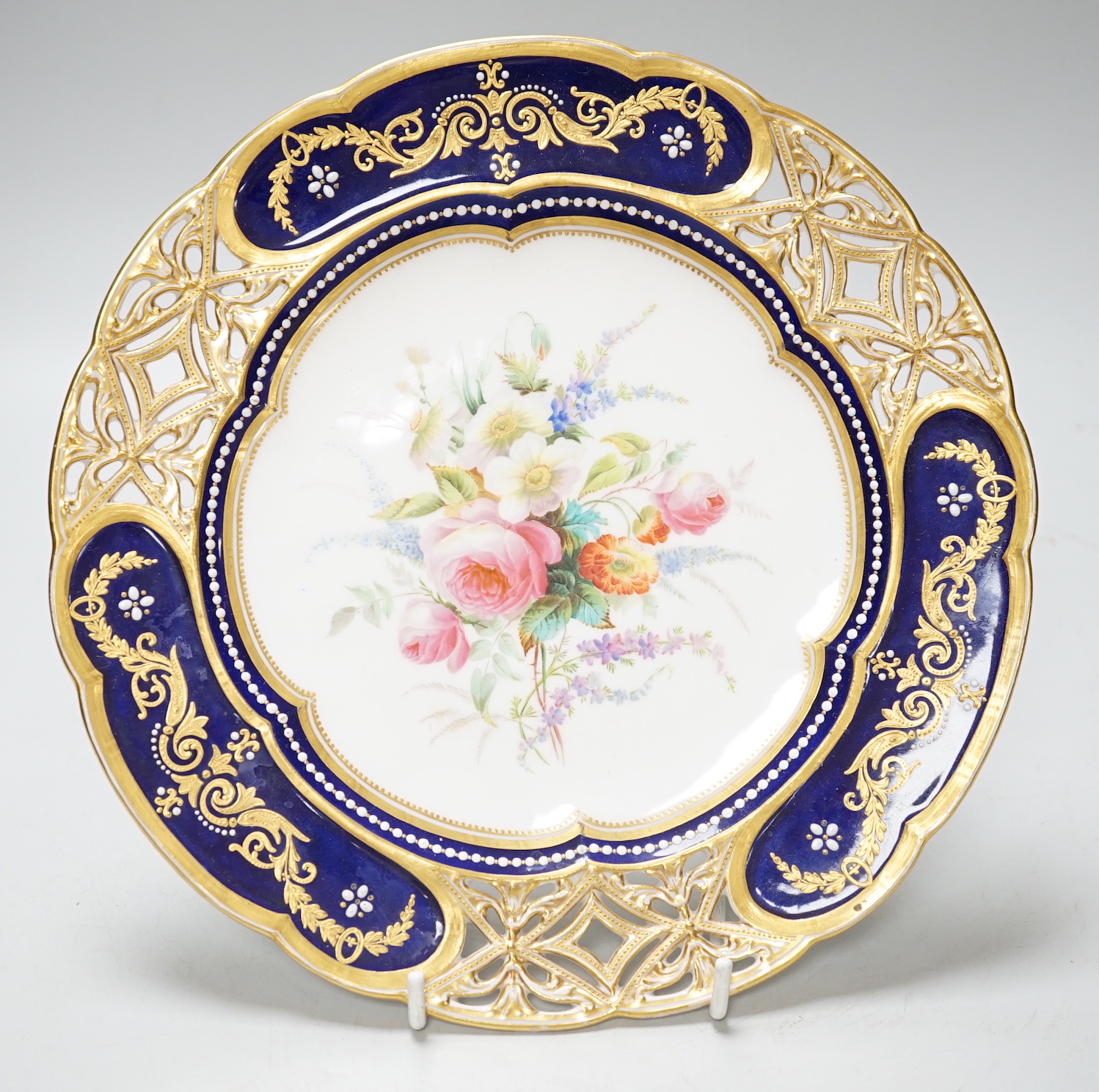 A Coalport plate with pierced border enamelled with white flowers and neo-classical raised paste gilding, the centre painted with bold flowers under jewelled inner border, ampersand mark